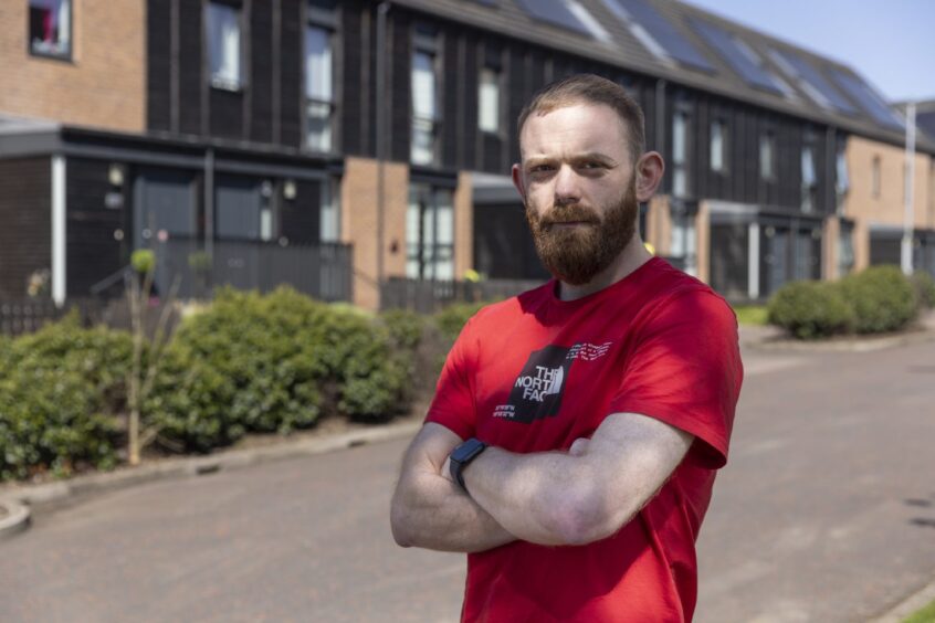 Tony McDermott, now aged 30, stands with the Athletes' Village as the back drop. He now works as a prison officer.