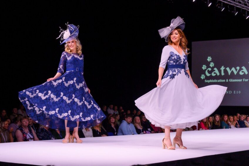 two women turn as they model wedding guest outfits on a catwalk