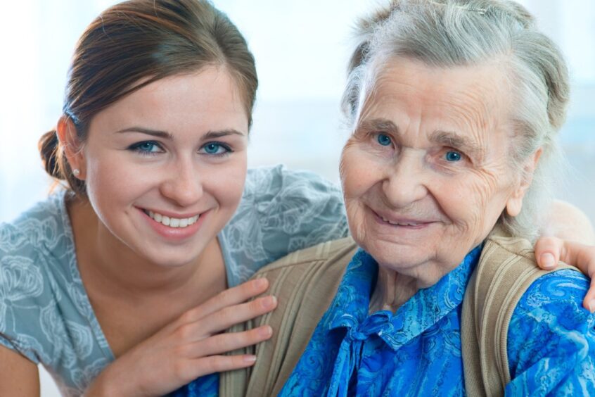 young woman smiles with her arms around a smiling elderly woman