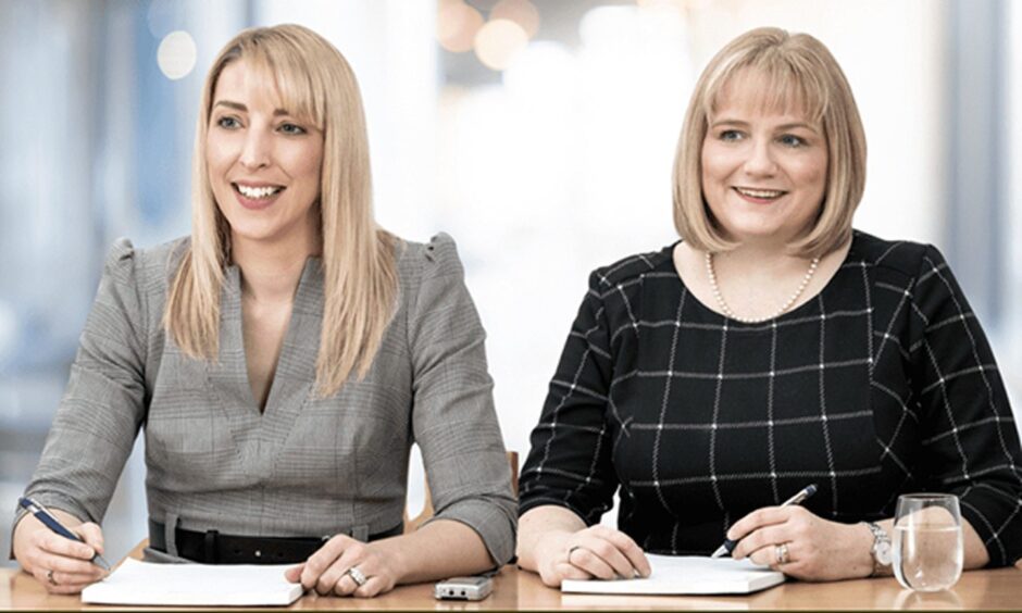 two women smile as they sit at a desk with papers in front of them