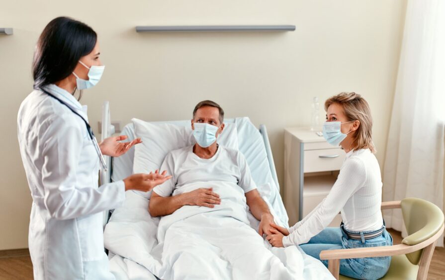 Doctor speaks to patient's wife at his bed.