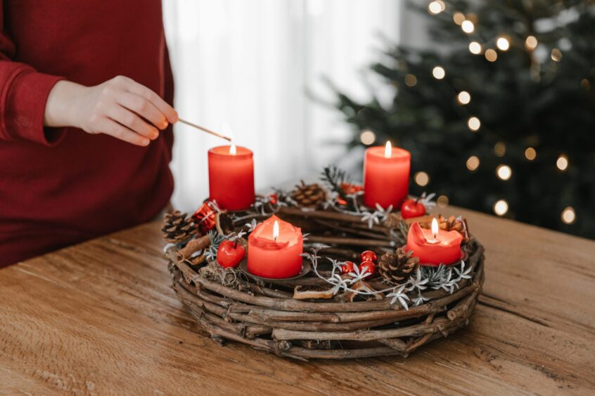 person lights candles on a holiday wreath adorning a table