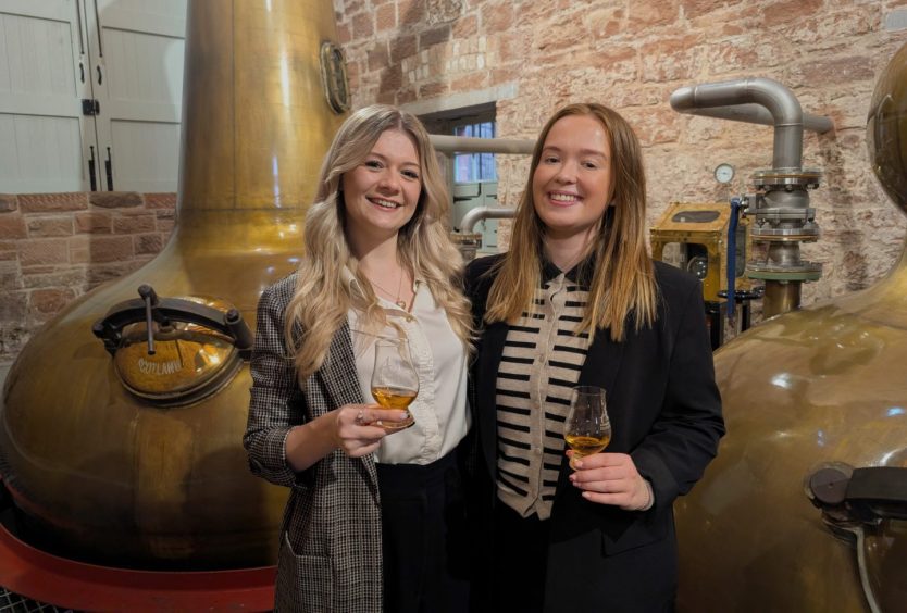 two femail staff members standing in front of the stills at annandale distillery