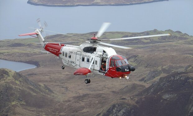 The red and white coastguard helicopter pictures flying over land, near the coast.