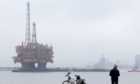 An oil rig being looked at by a man with a bilke from the shore
