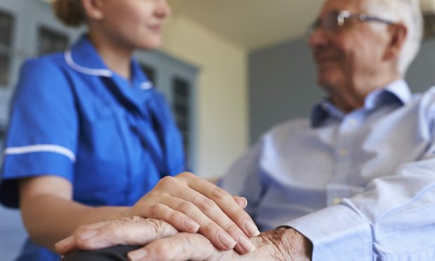 Nurse standing holding hand of old man sitting.