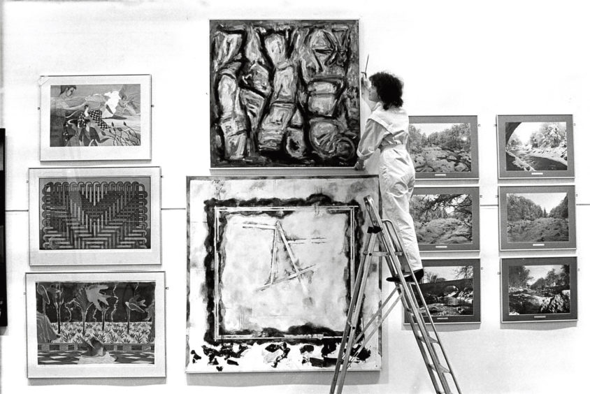 1986: Susan Begg hangs a large painting.