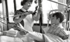 1968: A nurse smiles while she helps a boy with his leg in splints.