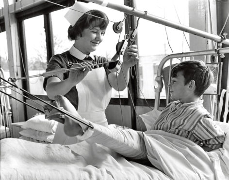 1968: A nurse smiles while she helps a boy with his leg in splints.