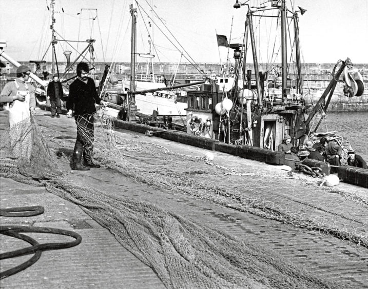 1975: Fishermen hard at work repairing nets in the sunshine at the harbour