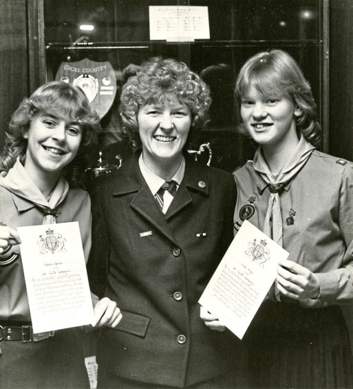 1984: Brownie Guider Dorothy Forbes of 1st Cults Pack presents awards to patrol leaders Karen Spence and Lisa Gray at Cults Academy hall