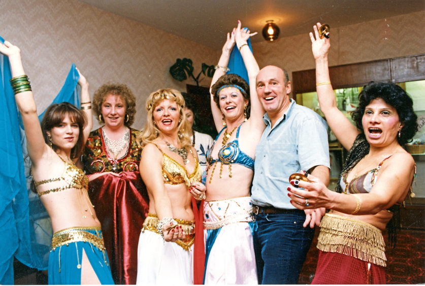 A man surrounded by women in exotic dancing costumes