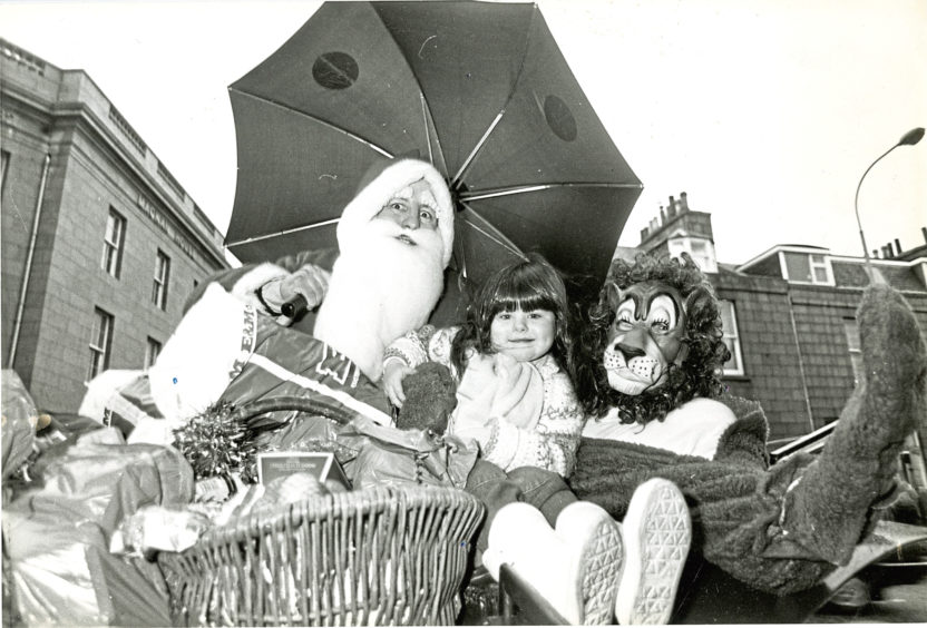 1986: Little Leanne Young, 4, shelters from the rain along with Santa Claus and Leo the Lion, who were on a stagecoach tour of Aberdeen city centre stores to collect Christmas gifts for the old and needy