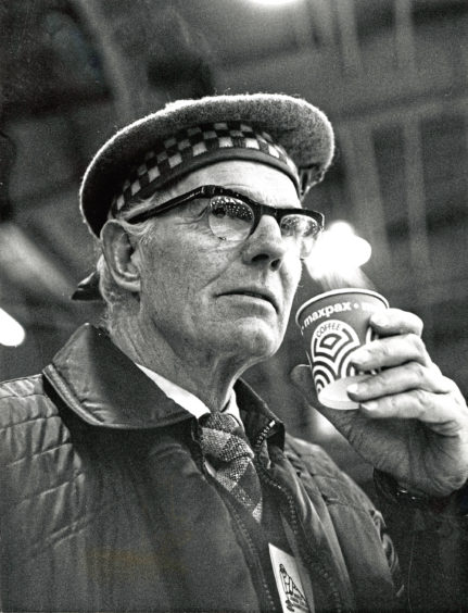 1976: Umpire John Carmichael takes precautions against the cold with a warming drink