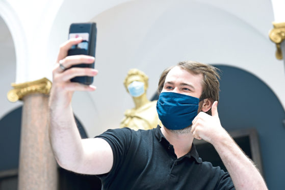 A museum assistant at Aberdeen Art Gallery takes a selfie with a masked statue of St George