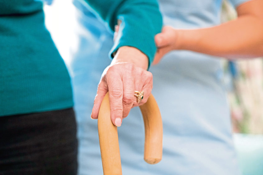 Woman with walking stick being supported by carer