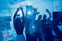 Group of modern young people dancing under confetti at private house party lit by blue light; Shutterstock ID 1050017789