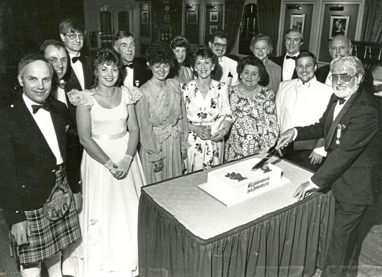 1987: The Lyric Musical Society of Aberdeen honorary president Mr George Low cuts their 35th anniversary cake in the Amatola Hotel while present and former member look on.