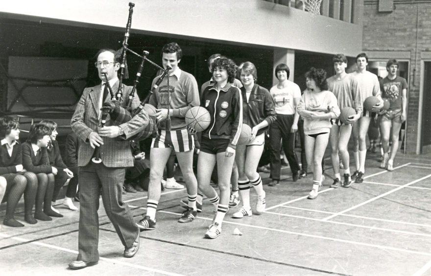 1983: These gladiators being piped into the arena by technical teacher Ron Gray are teachers and senior pupils who will take part in the IX Hazlehead Academy Lympic Games. The games opened with a basketball challenge. The staff won the match 18-16. The games go on all week with volleyball, water polo, hockey, football, table tennis, darts and badminton and the Lympic score to date stands at 5-3 for the pupils.