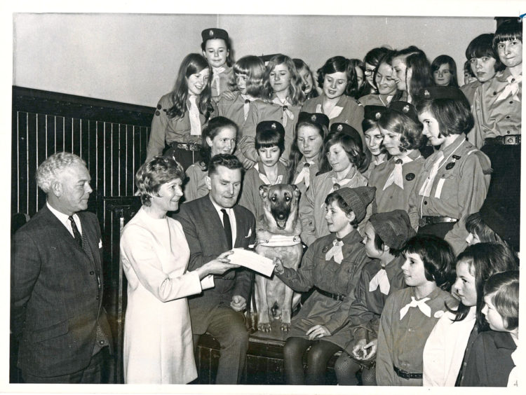 1970: Members of the 37th and 37th A Brownies, Guides and Rangers, Beechgrove Church, Aberdeen, look on as Brownie Janet Stewart, presents a cheque to Mr Alex Duguid, Guide Dogs for the Blind Association, at a ceremony in the church hall last night. With Mr Duguid is Pearl Murray, the Press and Journal woman's editor. The 37th are the first of the city Guides to reach their guide dog target. One of their group Jill Porteous, will take delivery soon of a puppy to be reared at her home before undergoing guide dog training. The puppy will be known as Diamond.