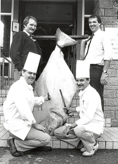 1988 - Chefs at the Stakis Tree Tops Hotel, Sandy  Flett, left, and Steve Pledger get their knives  ready for the 7½ stone halibut to be on the  menu at the Fish Festival dinner. Holding the  fish are Helge Korsager, left, of United Fish  Products, and Sandy Law, of Aberdeen Fish  Curers’ and Merchants’ Association