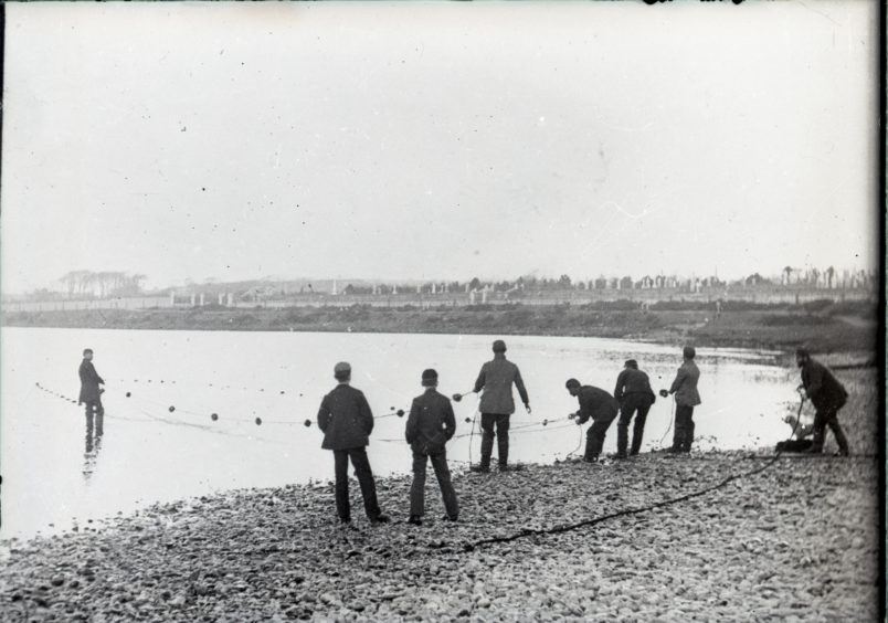 Group of men pulling fishing nets from river