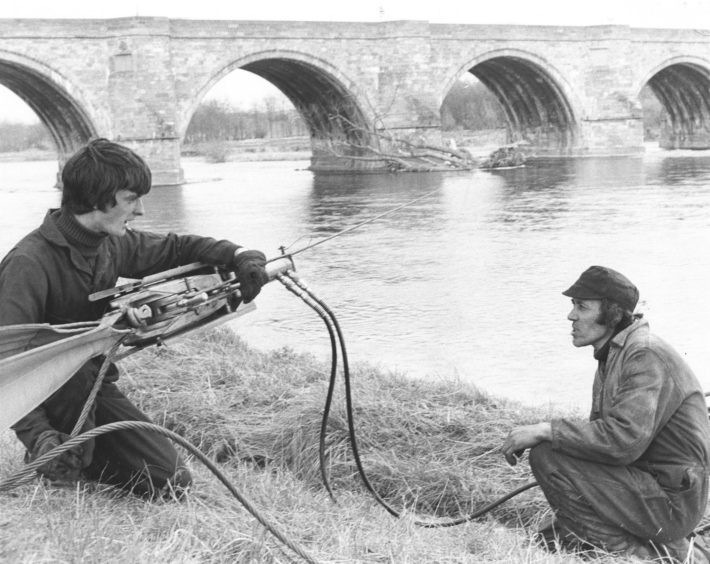 1979: Employees of Aberdeen firm Lifting Gear Hire Ltd., Riverside Drive, apprentice fitter Ian Nicol, and engineer Kenny Ross successfully winch a tree from the river at Bridge of Dee, Aberdeen, yesterday. The tree was washed downstream in the winter floods and had been lodged against the bridge for almost four months.