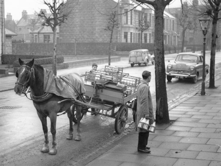 1962: Late morning in Aberdeen's West-end in January, 1962 and milk is being delivered in the ago-old way. Near the end of his round, a milkman from Kennerty's Dairy stops outside a house in Forest Avenue near the corner with Great Western Road to leave a crate of milk. The cash bag over his shoulder indicates he is also collecting the weekly payments from his customers.
