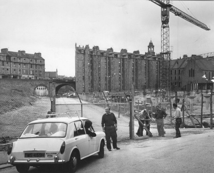 1971: With the end of the trades holidays and the weather more congenial, work was resumed yesterday on most of Aberdeen's building sites. This was the scene at the Upper Denburn as workmen sealed off a public road that has for years linked Woolmanhill and the southmost section of Rosemount. Now the entire Denburn development site has been fenced off to facilitate work on the two level car park, on top of which will be the city's first area health centre.