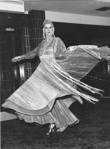 A model mid-spin, showing off the swaying fabric of the dress she's wearing. The dress has layers and tassels that create movement