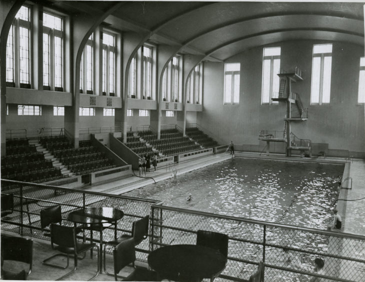 1955: A view of the interior of the Bon Accord swimming baths in Aberdeen looking towards the diving board. Seating areas are visible.