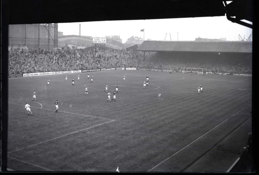 1957: A match in play at Pittodrie Park, Aberdeen, the home of Aberdeen FC.  A advert for the Aberdeen Evening Express Green Final edition can be seen in the distance.