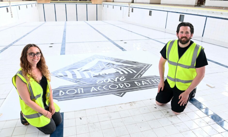 Trustees Fiona Stevenson and Steven Cooper by a Save Bon Accord Baths poster on the bottom of the cleaned pool.