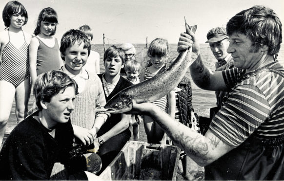 1984: A silver salmon from the nets at Aberdeen Beach holds the attention of youngsters and adults alike as fishermen Tommy Thomson and Bob Nicholson show the fish to the holiday makers