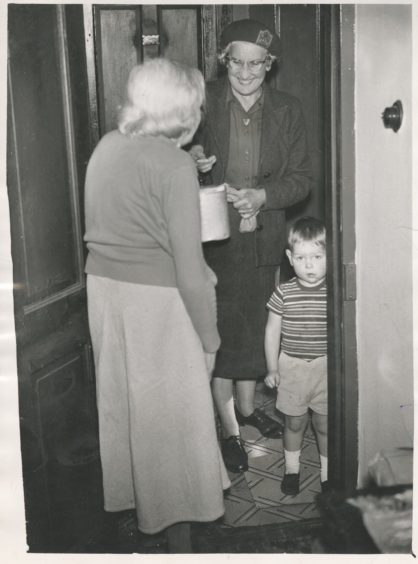 1961: A warm smile and a hot meal for Mrs G. Erskine, when Mrs B. Crawley of the WRVS calls at the door. Also pictured is Stephen Gibb (3), a neighbour of Mrs Erskine's.