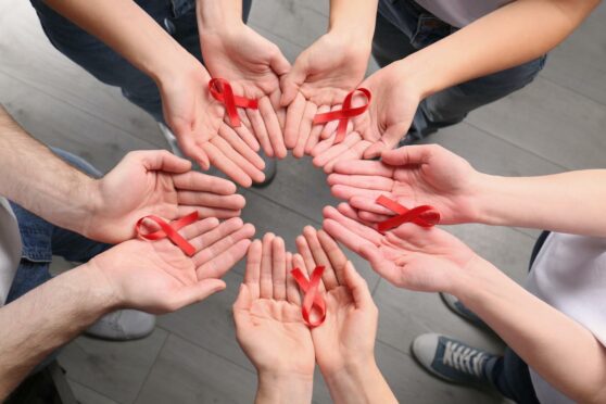 Detail of hands with red ribbons for World Aids Day and the importance of going for a HIV test in Aberdeen