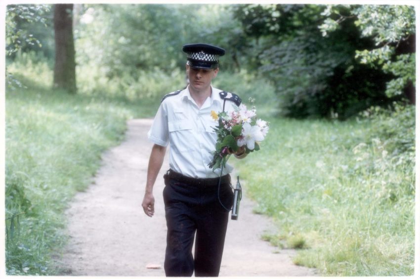 A policeman carrying floral tributes near the scene of Rachel's murder in 1992. 
