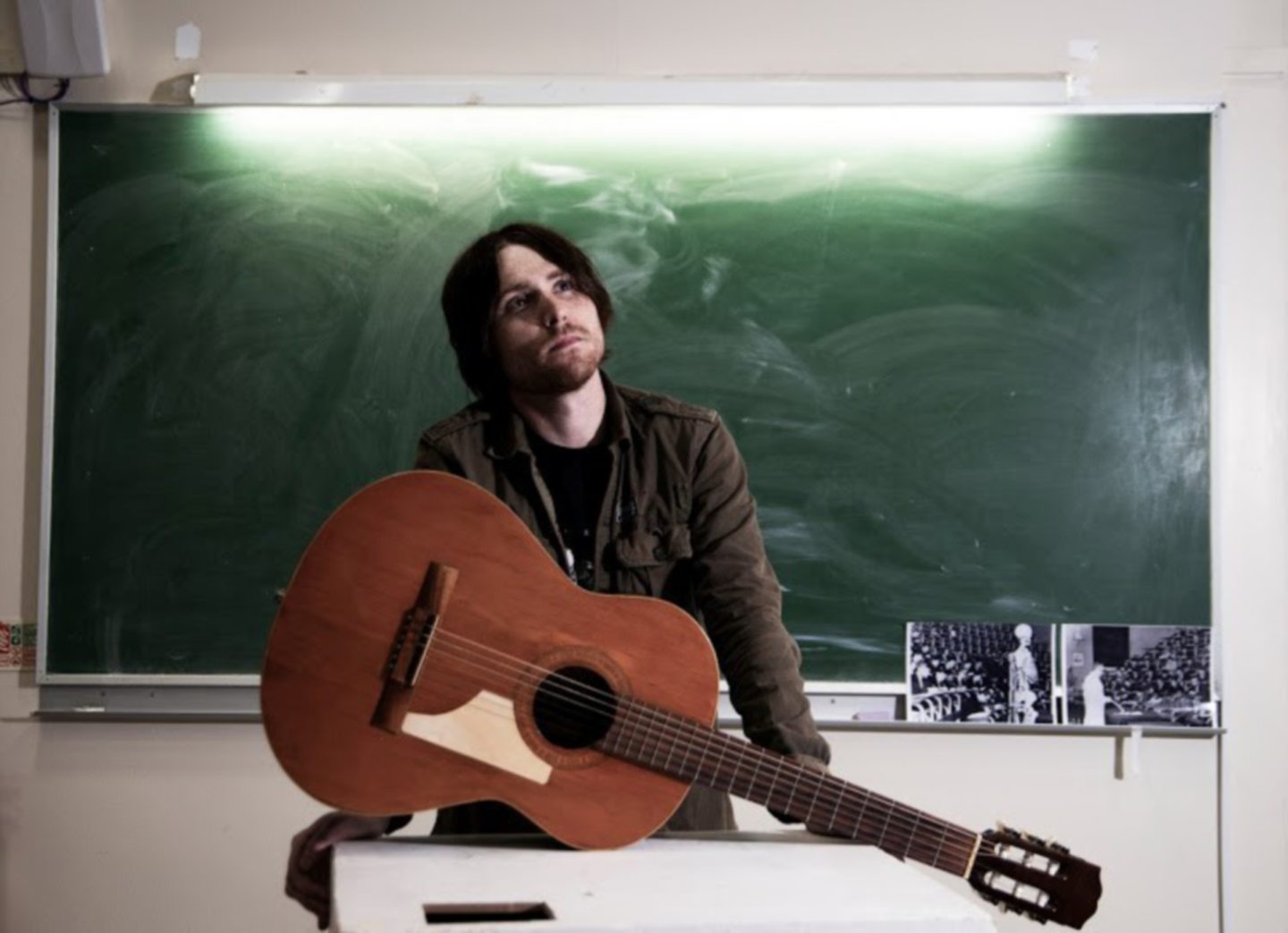 Aberdeenshire musician Craig John Davidson holding a guitar while appearing to daydream in front of a school blackboard. Supplied by Paul Nicol