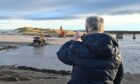 A beach-walker stops to take a picture of construction underway on the Lossiemouth bridge.