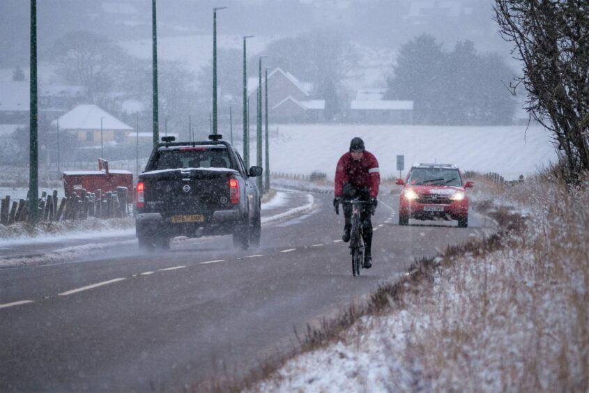 Cyclist on a snowy road at Bonar Bridge, Scotland.