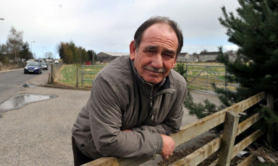 Alastair Kennedy, leaning on a wooden fence with traffic behind.