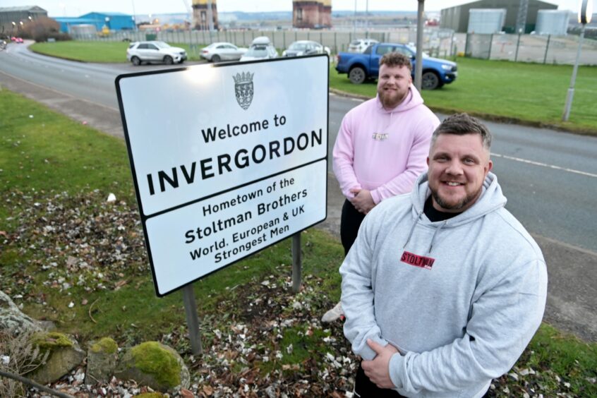 Luke and Tom Stoltman in front of 'Welcome to Invergordon' sign.