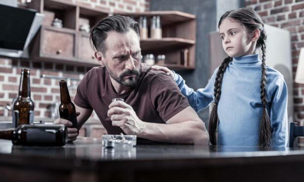 Little girl watching father get drunk alone at the table