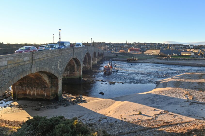 The digger working in the water while cars cross Banff Bridge