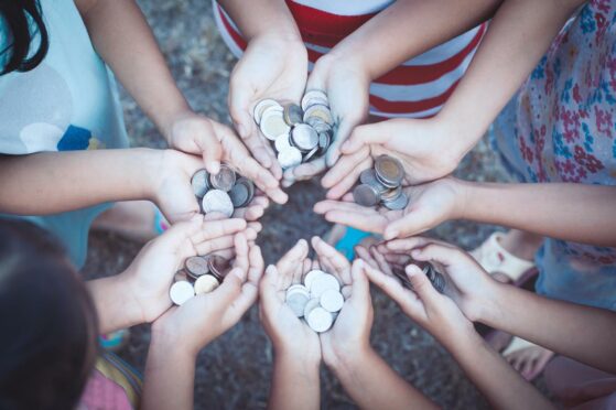 Children's outstretched hands holding coins in a circle