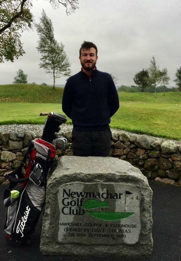 Adam Giles behind a Newmachar Golf club sign with his equipment to the side. 