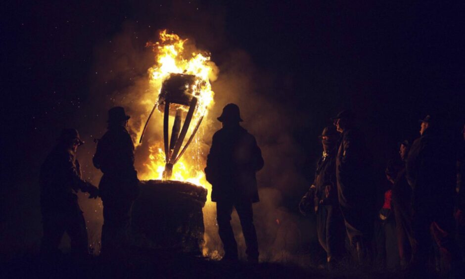 Silhouetted figures stand around the burning Clavie.