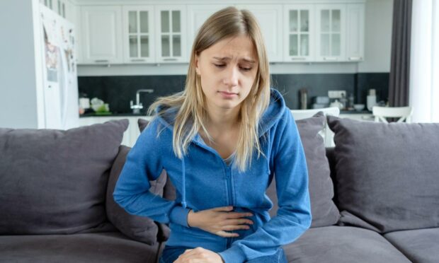 Woman sitting in the couch, holding her lower stomach in pain