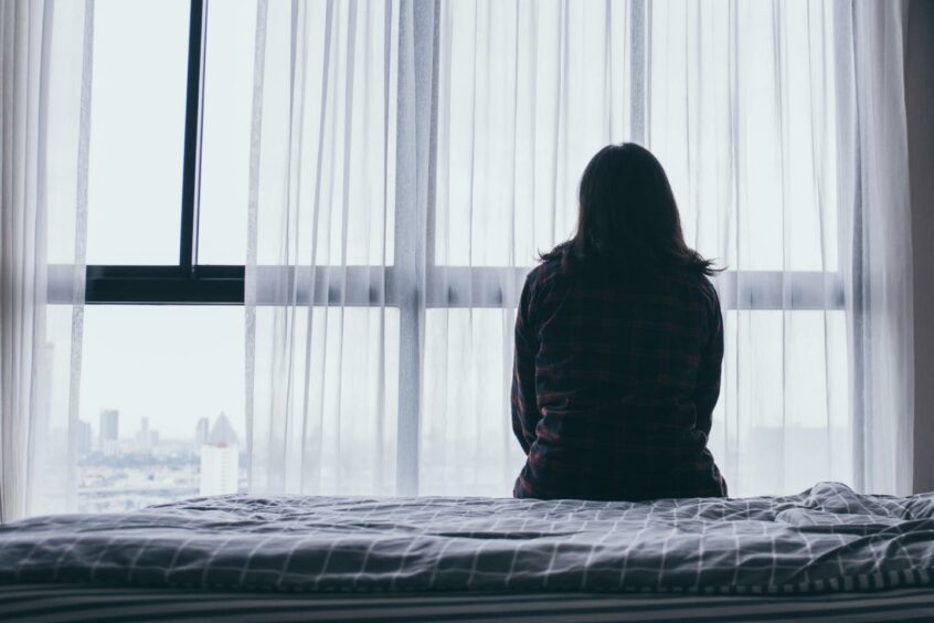 Woman sits on the side of her bed. 