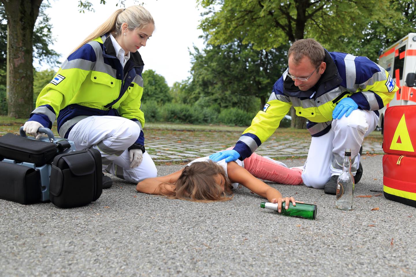 Two paramedics tending to a drunk woman collapsed on the ground with a bottle of alcohol in her hand
